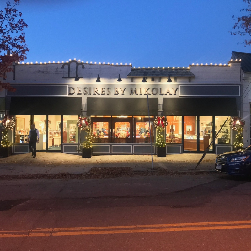 Commercial holiday lighting on downtown retail storefront with roofline lights, wreaths, and illuminated entrance planters