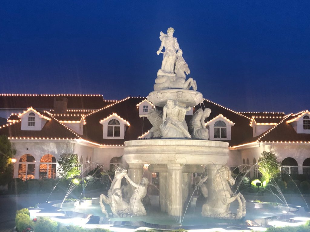 Commercial Christmas light installation featuring illuminated rooflines and a decorative fountain at a property in New Rochelle, NY.