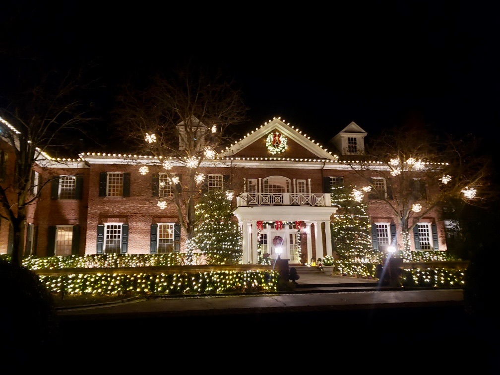 Residential Christmas light installation with warm white roofline lights, decorated trees, and a brick home.